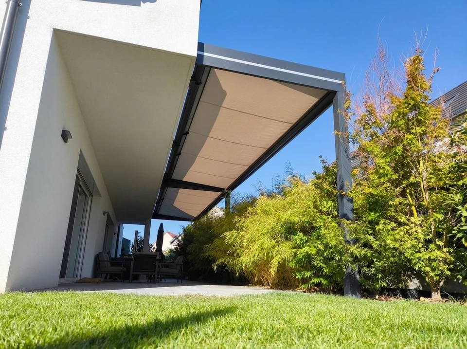Terrasse extérieure couverte par une pergola bioclimatique à toiture rétractable en toile beige tendue sur structure aluminium anthracite autoportée