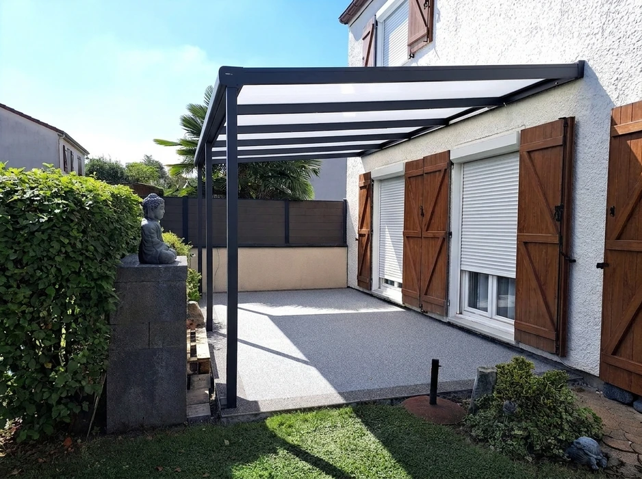 Terrasse extérieure couverte par une pergola bioclimatique en aluminium anthracite, adossée à une maison