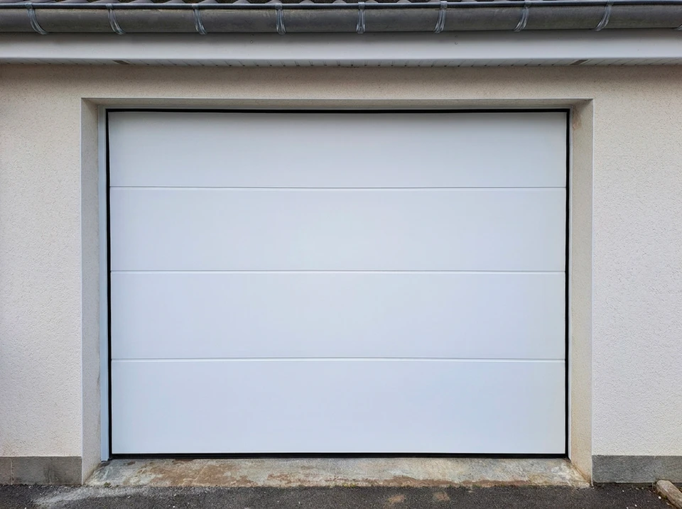 Porte de garage battante à deux vantaux en bois massif, ouverte partiellement, montée sur une façade résidentielle en enduit blanc, encadrement de garage en brique apparente, menuiserie extérieure d'une maison individuelle.