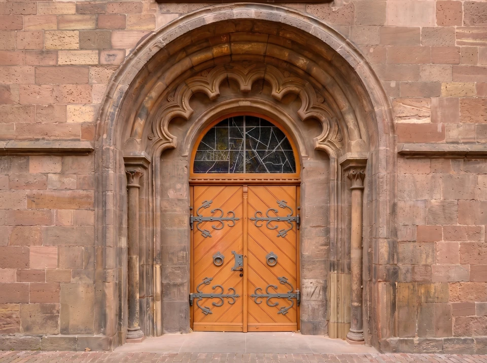 Porte d'entrée en bois massif de couleur miel clair, style haussmannien années 1890, encadrement en pierre de taille beige sculptée avec moulures, panneaux supérieurs et inférieurs rectangulaires aux portes, poignée ancienne en laiton patiné, serrure centrale ornementée laiton, imposte vitrée à petits carreaux, façade en pierre de taille restaurée.