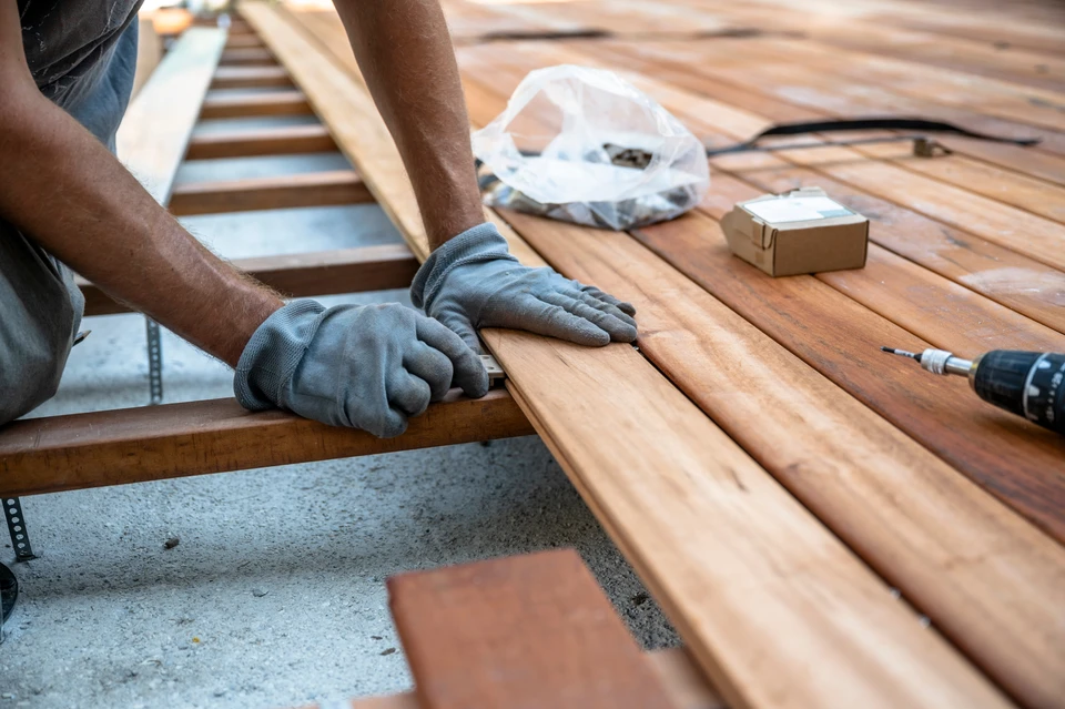 Homme en tenue de travail installant une terrasse extérieure, utilisant un niveau à bulle pour vérifier l'alignement des lambourdes en bois