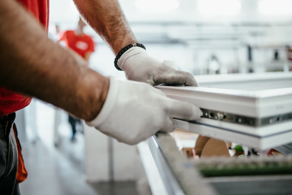 Artisan menuisier au travail sur un chantier, en train d'installer une porte d'entrée en bois massif dans l'encadrement d'une façade. L'artisan porte des vêtements de travail adaptés, utilise des outils professionnels (perceuse, visseuse ou tournevis). Vue en gros plan sur l'action d'installation, montrant la précision et le savoir-faire. Cadre de chantier réel, luminosité naturelle.